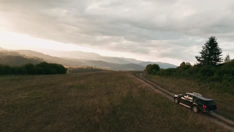 Imágenes-De-Drones-De-Carreras-Aéreas-Siguiendo-A-Un-Camión-4x4-Conduciendo-Lentamente-Por-Una-Carretera-Sin-Pavimentar-En-Un-Hermoso-Paisaje-Natural-Iluminado-Por-El-Sol-Con-árboles-Que-Proyectan-Largas-Sombras