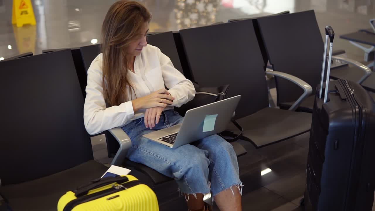 mujer moderna de cabello largo se sienta en la sala de salida y utiliza una computadora portátil para trabajar en el aeropuerto. chica turista freelancer trabaja y espera