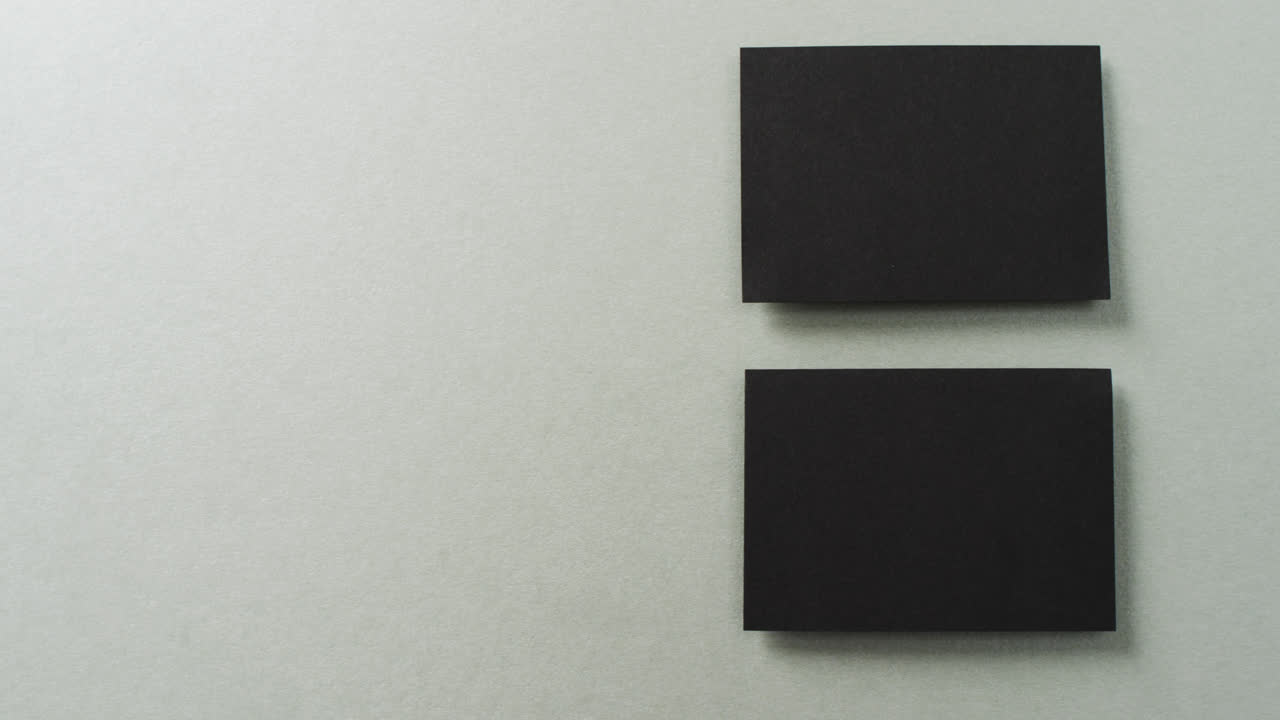 Overhead view of two black business cards arranged on grey background, copy space, slow motion