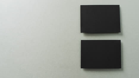 Overhead-view-of-two-black-business-cards-arranged-on-grey-background,-copy-space,-slow-motion