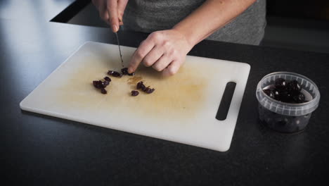 Woman-slicing-cherries-on-a-white-cutting-board-in-her-kitchen-as-she-prepares-to-make-mince-pies-for-a-holiday-dessert