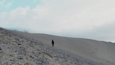 wide shot of a woman dressed in black in the desert looking around in the middle of nowhere with the wind blowing hard