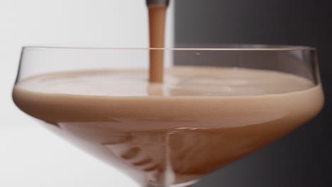 Primer-Plano-De-Espresso-Que-Se-Vierte-En-Una-Copa-De-Martini-Con-Un-Fondo-Mitad-Negro-Y-Mitad-Blanco,-Burbujas-Espumosas