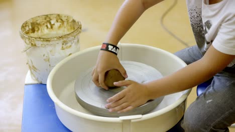 a boy works a lump of clay on a potter's wheel in the workshop