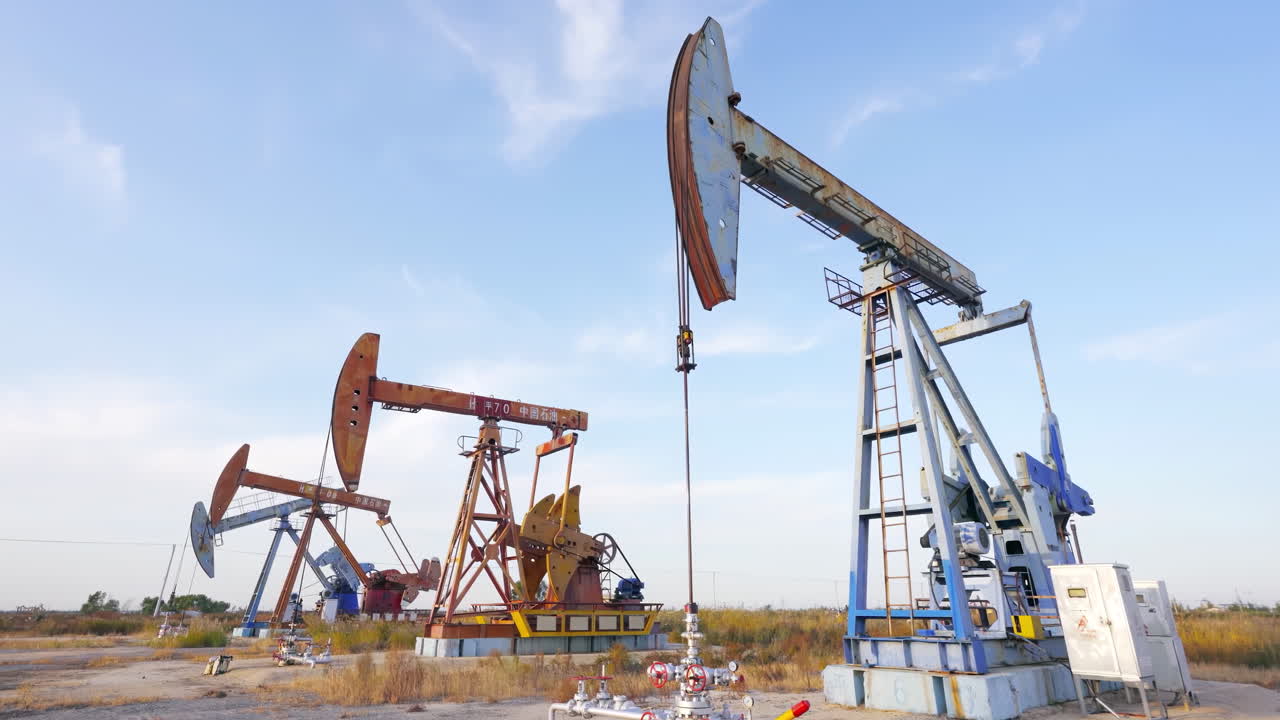 En råoliepumperamme er i drift i et ørkenoliefelt ved solopgang i et industrilandskab, med olieborerigge og borebukke. Råolieindustrien skaber energiforventninger og anvender pumperigge