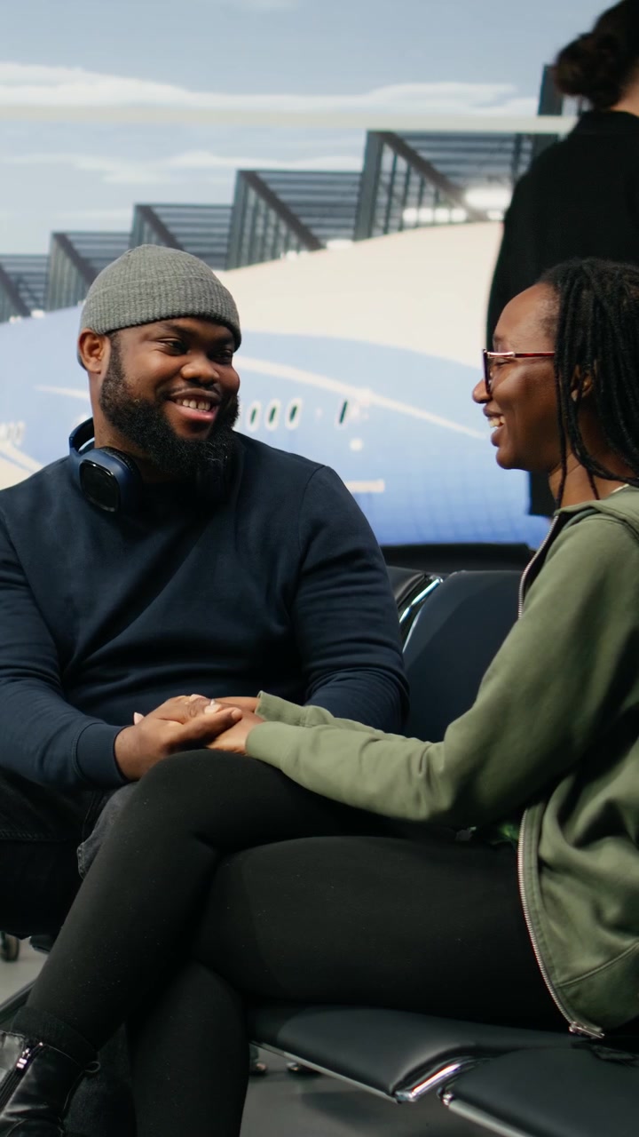 Vertical Video African american lovers laughing together seated in airport terminal