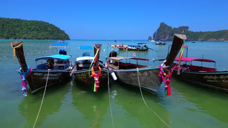 Koh-Phi-Phi-Bay,-colorful-traditional-longtail-boats-are-floating-on-calm-turquoise-water