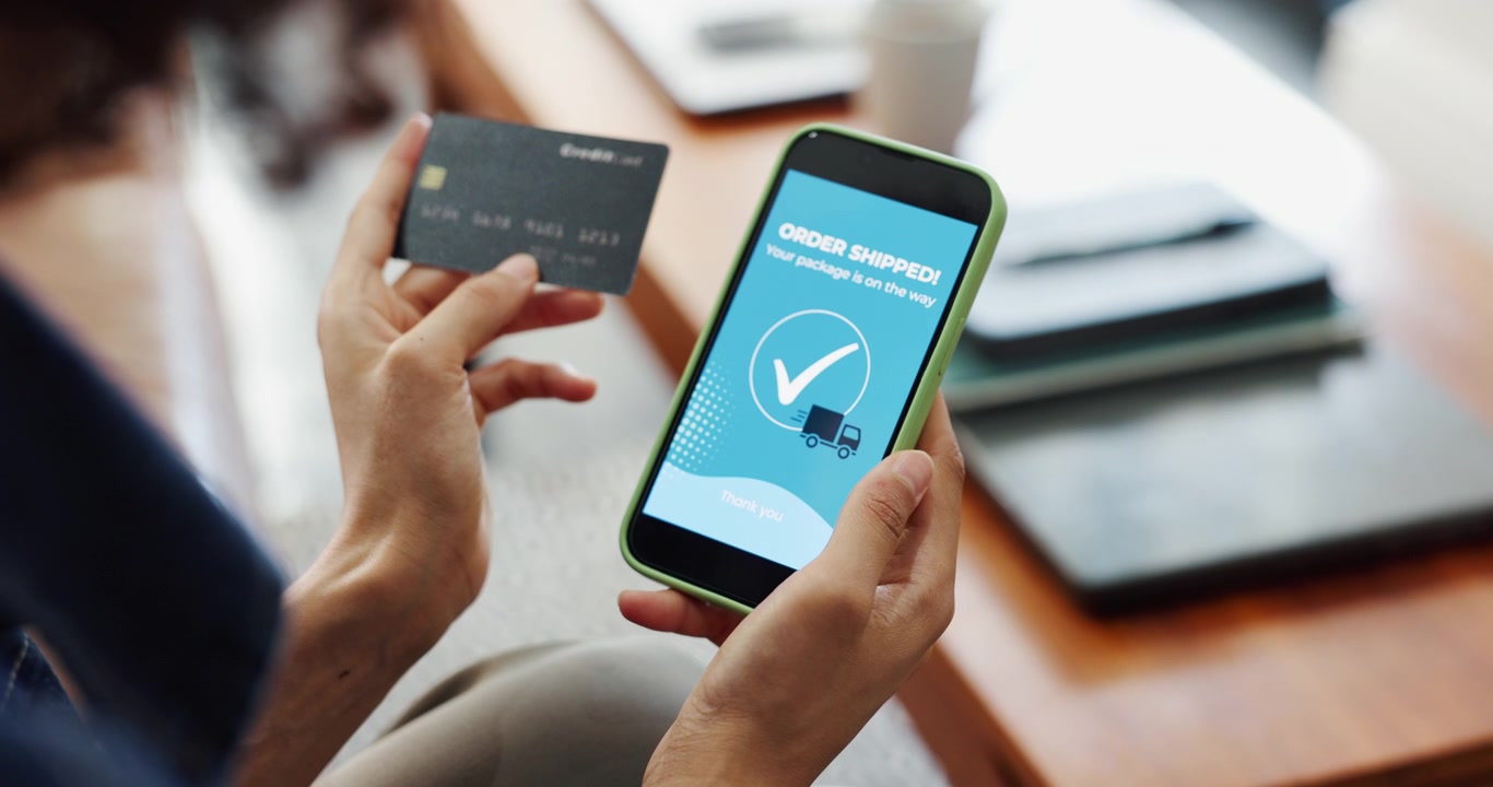 Person Holding Credit Card and Smartphone Showing Order Shipped Confirmation