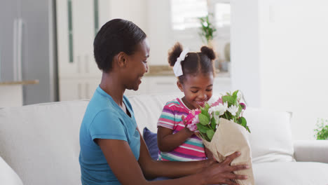 Feliz-Madre-E-Hija-Afroamericana-Sentadas-En-El-Sofá-Y-Oliendo-Flores