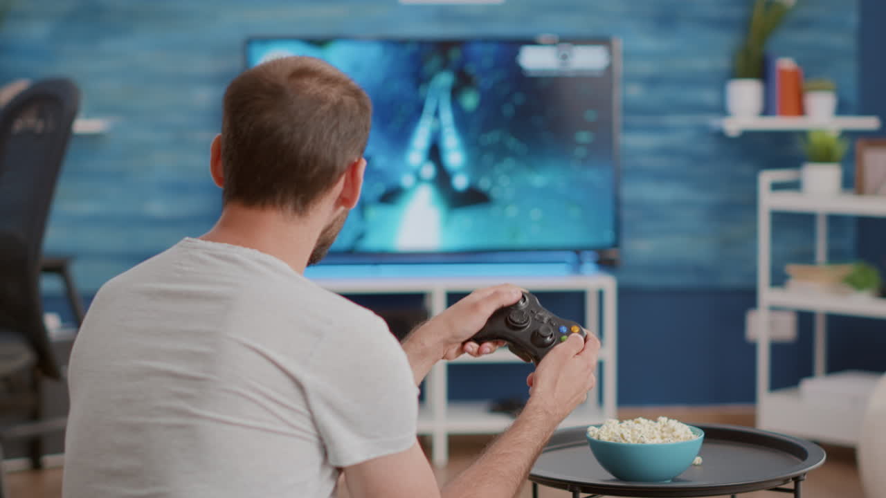 Uomo seduto sul divano che gioca a un videogioco per console sulla TV con un controller wireless