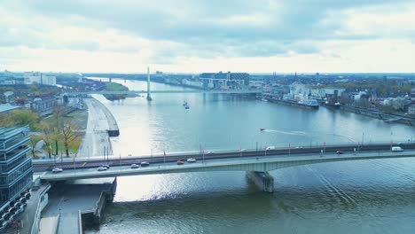 Drone-shot-flying-over-the-Rhein-river-in-Cologne,-Germany-on-a-cold-Autumn-morning-with-a-bridge-and-a-speed-boat-in-the-scene