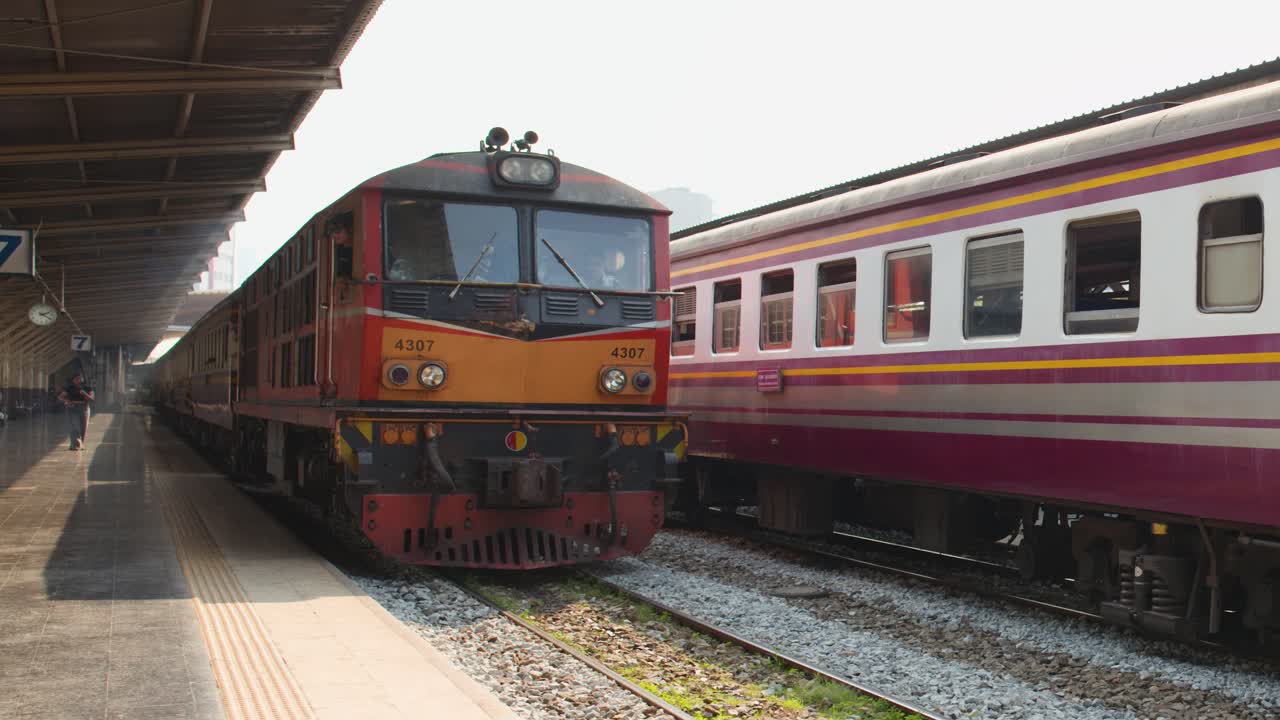 Lokomotif diesel merah menarik gerbong penumpang melewati peron tertutup di stasiun Hua Lamphong