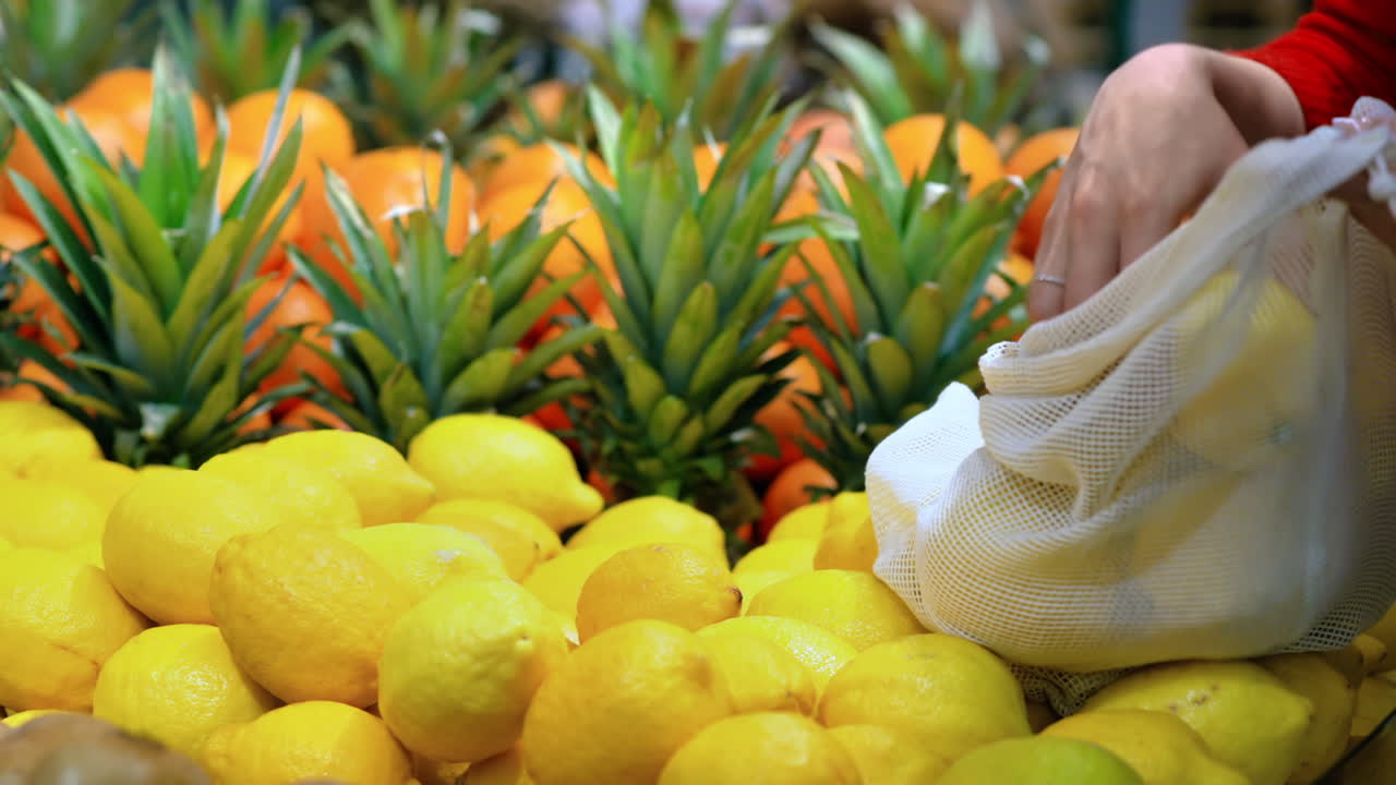 Woman picking lemons in a reusable bag in a store. Ecology and Earth Day thematics
