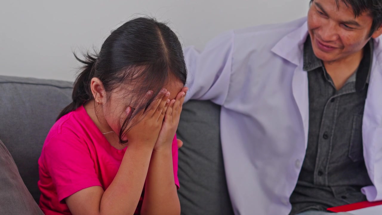 Little Asian girl covering her face and crying bitterly during therapy session