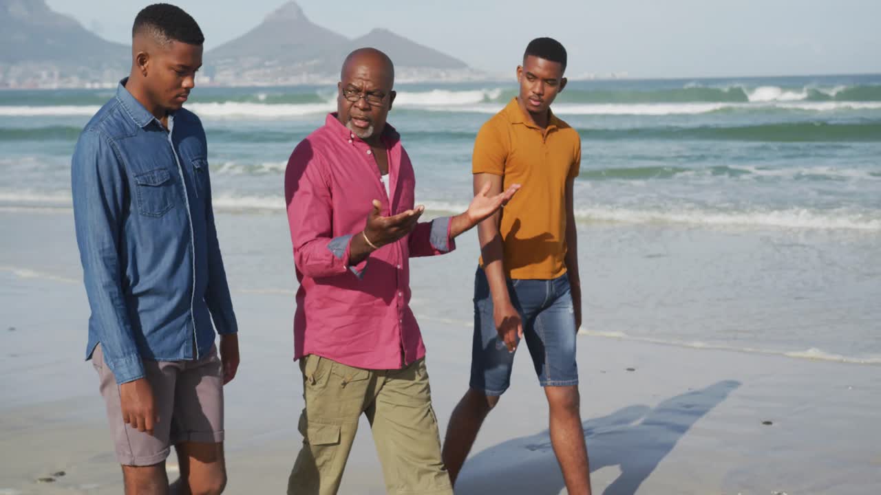 아프리카계 미국인 노인 아버지 와  ⁇ 둥이 십대 아들 들 이 해변 에서  ⁇ 고 이야기 하고 있다