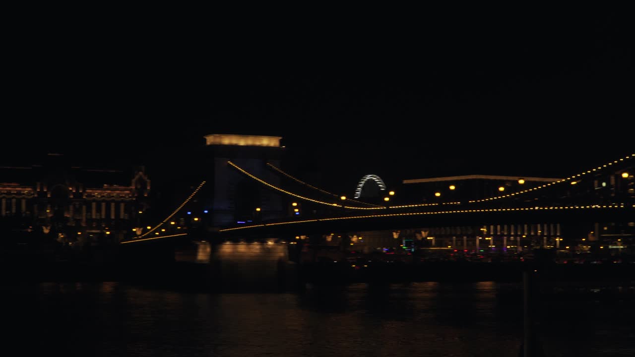 The Historic Stone Chain Bridge In Budapest Hungary Captures The Stunning Beauty Of The City During Evening With Lights And Peaceful Water Below - Wide Shot