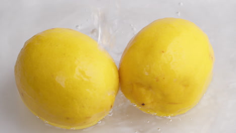 gotas de agua fluyen hacia limones amarillos en cámara lenta