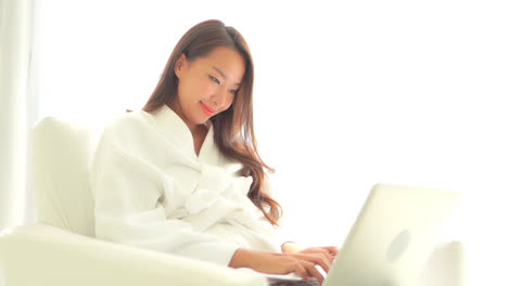 테리 옷을 입은 젊은 여성이 호텔 스위트룸의 특전을 즐기며 노트북 작업을 하고 있습니다.