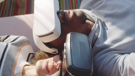 multiethnic couple in vr headsets lying on sofa and talking