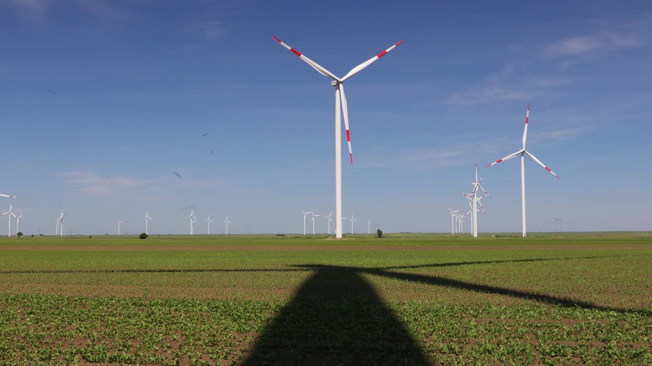Long shadow under windmill, large wind power turbines spinning to generating clean, green, renewable energy