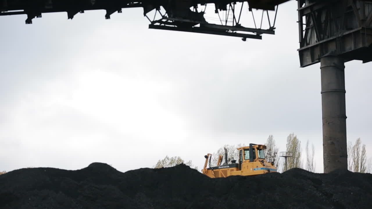 Warehouse of coal inventory plant. Yellow tractor loading the coal on the warehouse