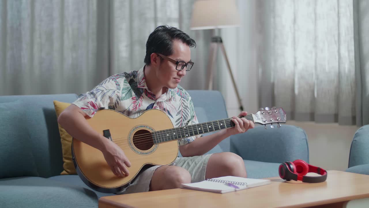 노트북을 들고 집에서 기타를 연주하는 아시아인 작곡가