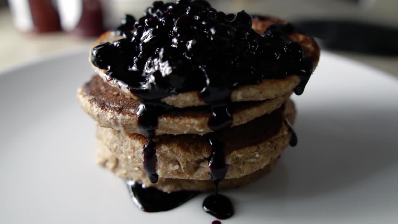 Garnishing four stacked pancakes with blueberry sauce