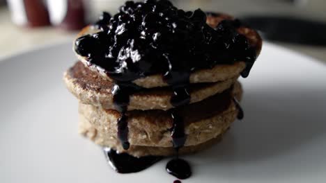 garnishing four stacked pancakes with blueberry sauce