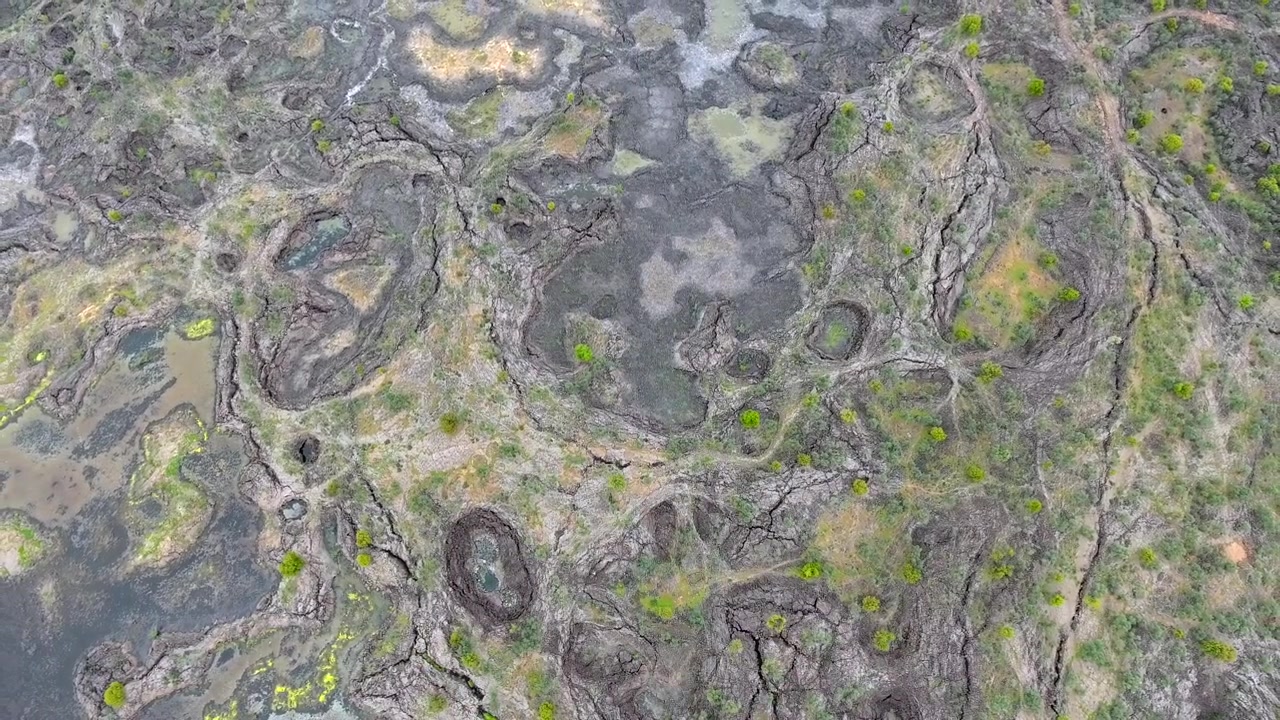 Luftfoto af vulkanlandskab med sprukken jord og sparsom vegetation