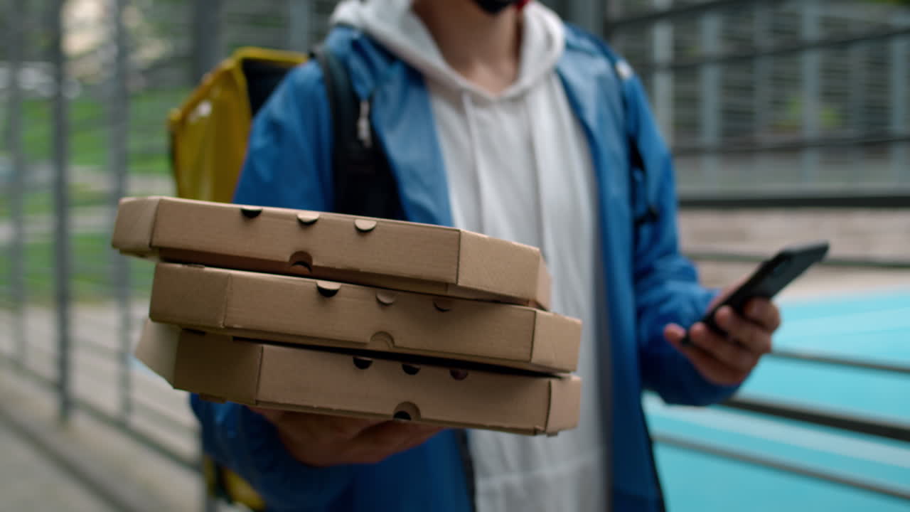 Pizza delivery person holding boxes and using smartphone