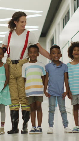 video of happy caucasian female teacher and class of diverse people standing at school hall