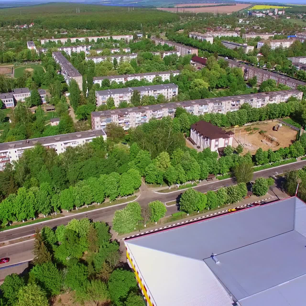 Large roof of a rectangular building in the city. Residential areas with lots of green trees. Aerial perspective