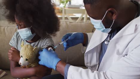 african american doctor vaccinating crying african american girl wearing face mask