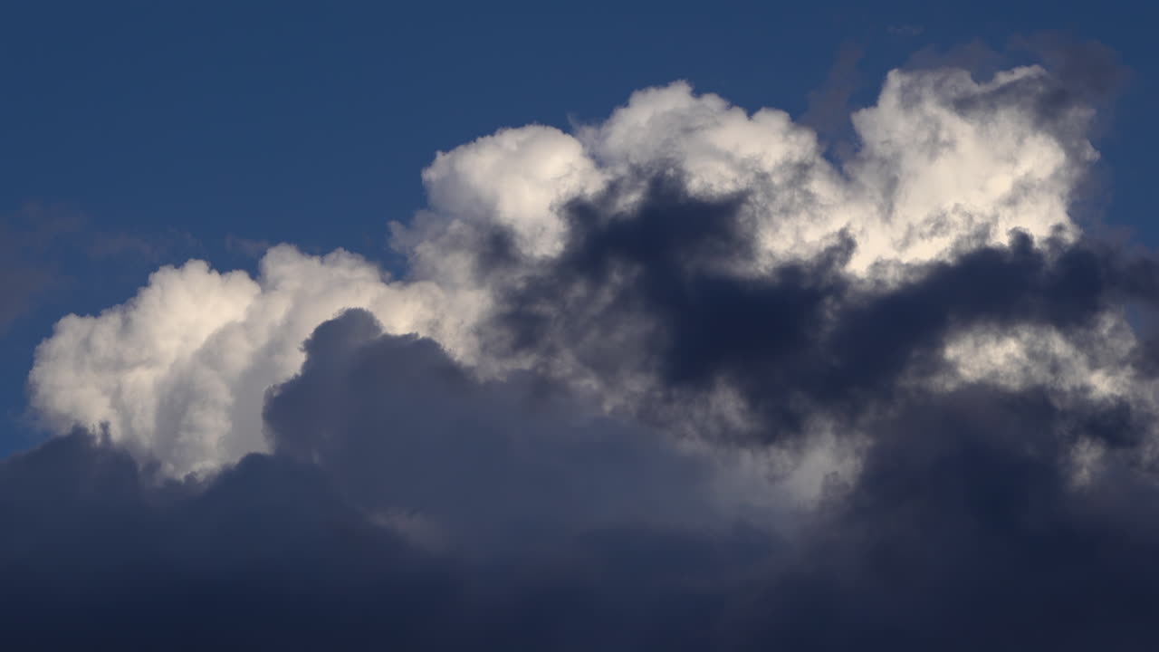 Sunlit white cloud rising above a layer of darker clouds against a deep blue sky