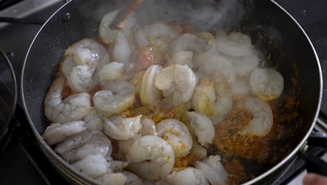 stirring fresh prawns with wooden spoon with hot, bubbling sauce in a pan