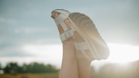 close-up of legs in white sandals raised against warm sunlight glow, soft blur background features trees in distance, creating relaxing, peaceful outdoor setting with golden light and natural vibes