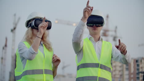 Two-people-in-virtual-reality-glasses-on-the-background-of-buildings-under-construction-with-cranes-imitate-the-work-of-the-interface-for-the-control-and-management-of-construction.