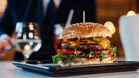 gourmet burger featuring a juicy patty, melted cheese, pickles, fresh lettuce, tomato, and onion on a sesame seed bun, enjoyed by a businessman in a restaurant setting