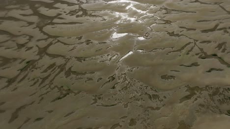 Aerial-ascending-birdseye-view-of-the-muddy-tidal-flats-of-Slikken-van-voorne-with-small-pools-of-water-reflecting-the-light-of-the-sun