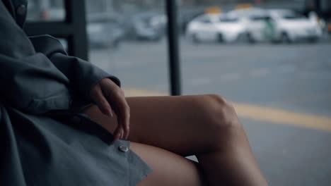 Woman-sitting-bus-station-in-urban-area-near-highway-road-on-daytime.