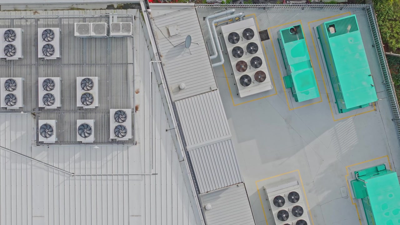 Drone footage captures a high-angle view of a contemporary data center’s rooftop lined with HVAC units, ventilation fans, and industrial equipment on a bright, clear day.