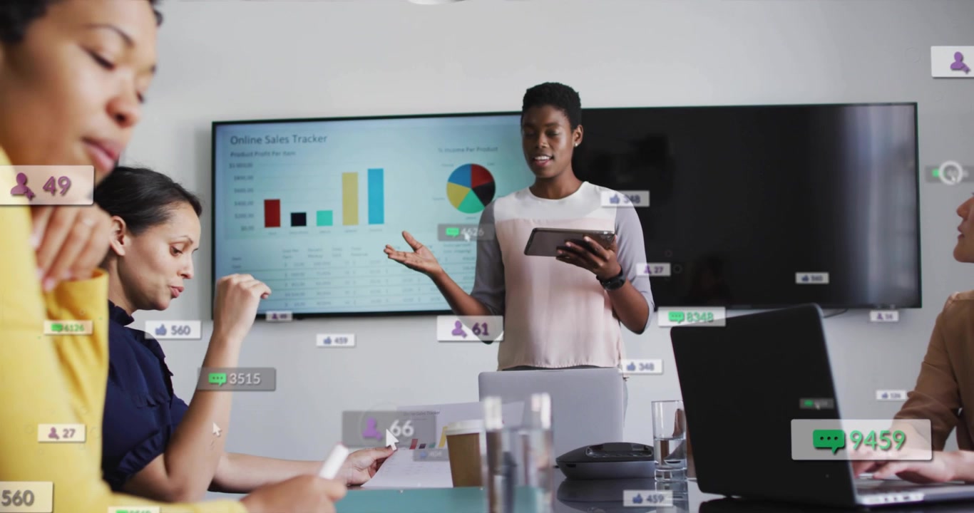 Presenter gesturing with tablet at conference table, initiating UI online sales charts for update