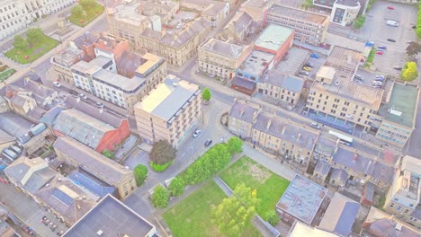 high-angle drone view over barnsley town centre in south yorkshire, england, showing historic stone buildings, streets, and a small green park illuminated by soft daylight