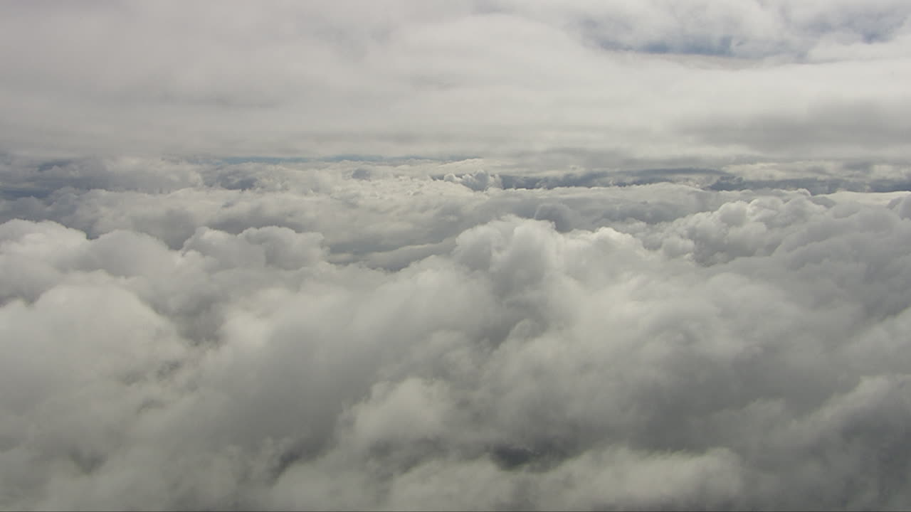 Aerial dolly shot above dense clouds with gaps showing the snow-covered fields below