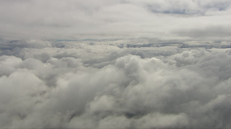 Aerial dolly shot above dense clouds with gaps showing the snow-covered fields below