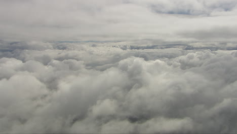 Luftaufnahme-Eines-Dollys-über-Dichten-Wolken-Mit-Lücken,-Die-Die-Schneebedeckten-Felder-Darunter-Zeigen