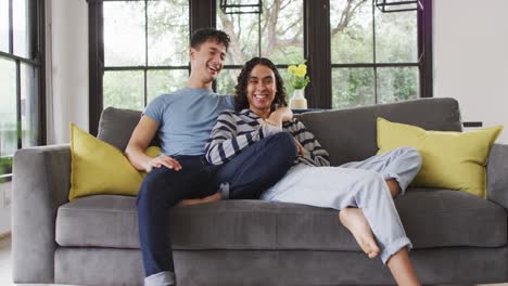 retrato de una feliz pareja masculina diversa sentada en el sofá y abrazándose en la sala de estar