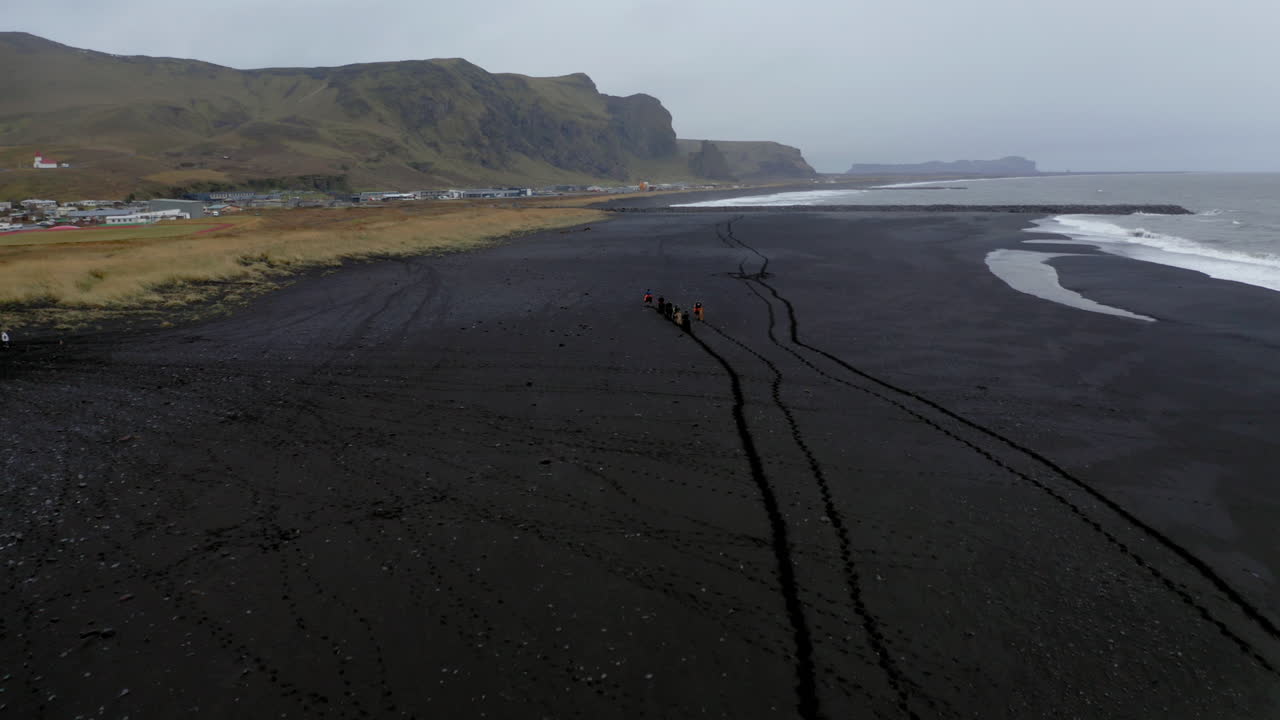 antena: volando hacia un grupo de turistas a caballo en la playa de arena negra de vik en islandia