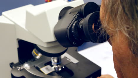 un científico mirando a través de la lente de un microscopio a las células cancerosas humanas en un laboratorio de investigación de biología médica
