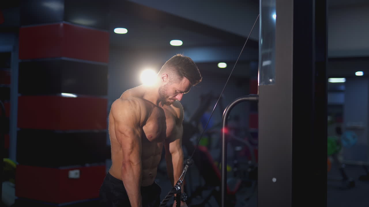 Athletic guy pumping his muscles. Shirtless bodybuilder training his sportive body in the gym. Side view. Sportive lifestyle.